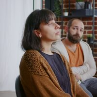 Woman sharing sad story with people and psychologist at aa group therapy session. Person dealing with addiction, talking to patients in circle at rehabilitation program meeting.